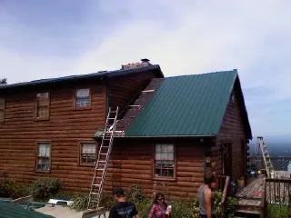 Green metal roof going on a two story log home with ladders set in Venus